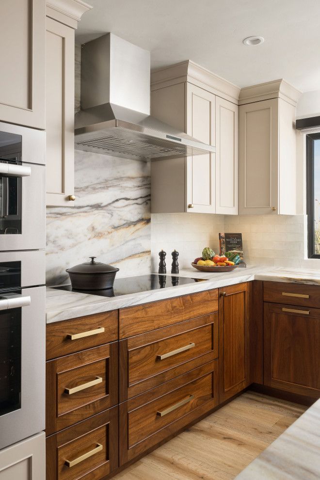Modern kitchen with beige and wood cabinets, marble backsplash, stainless range hood, and light wood floor