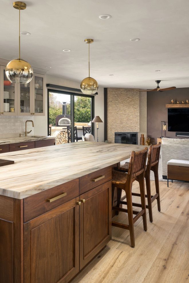 Modern kitchen with wood island, bar stools, gold pendant lights, and view of a bright dining area