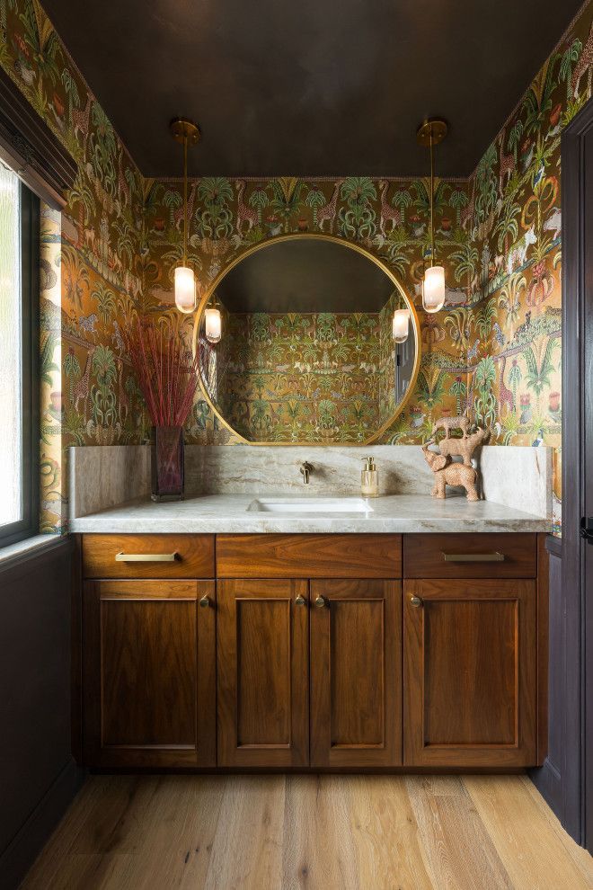 Vintage bathroom vanity with a marble countertop, round mirror, and colorful floral wallpaper