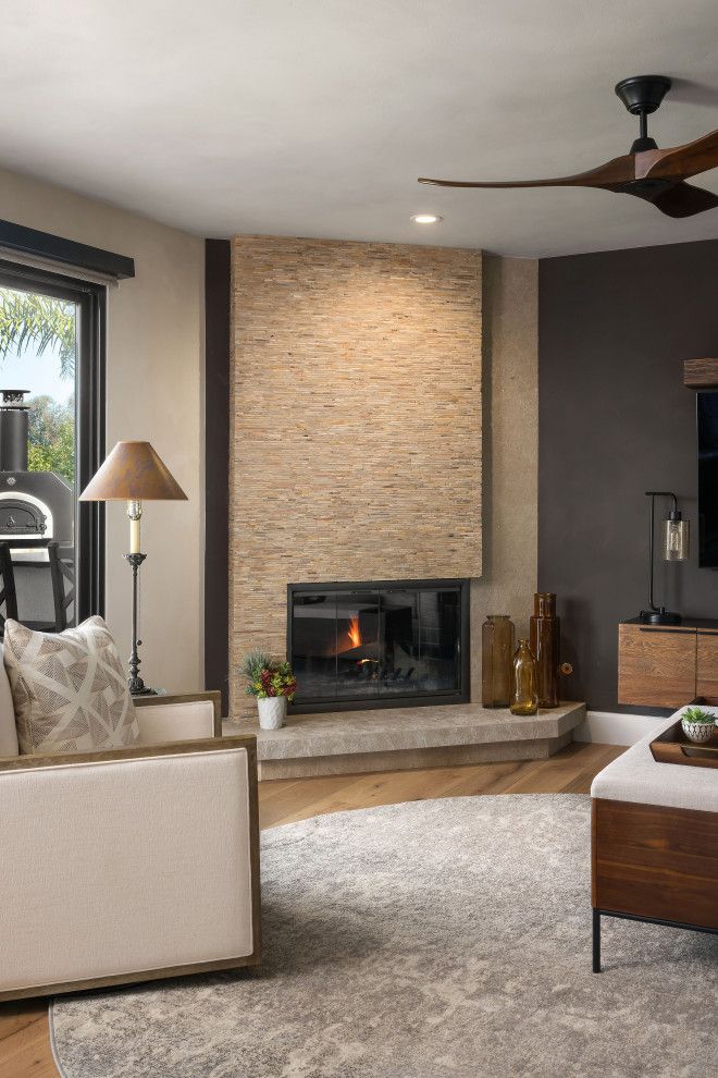 Modern living room with a stone fireplace, neutral sofa, and ceiling fan under soft natural light
