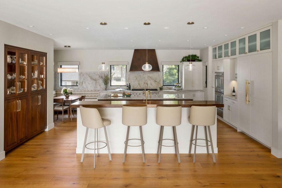 Bright modern kitchen with a large island, white cabinetry, wood floors, and stainless steel appliances