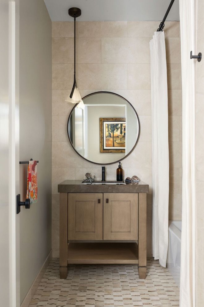Small bathroom with wooden vanity, round mirror, wall sconce, and white shower curtain.