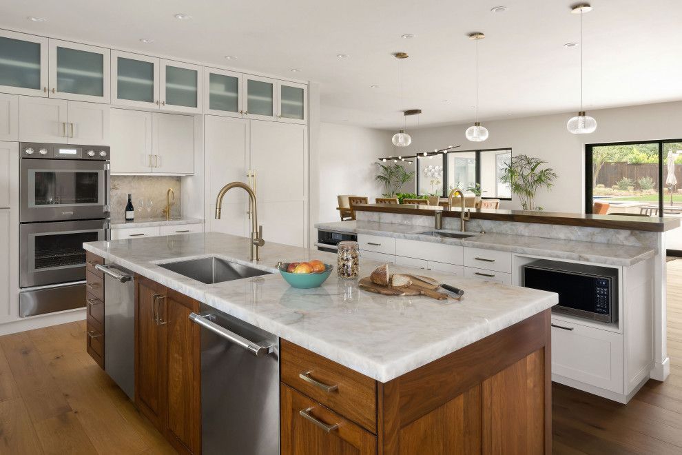 Modern kitchen with white cabinets, marble island, stainless appliances, and large windows.
