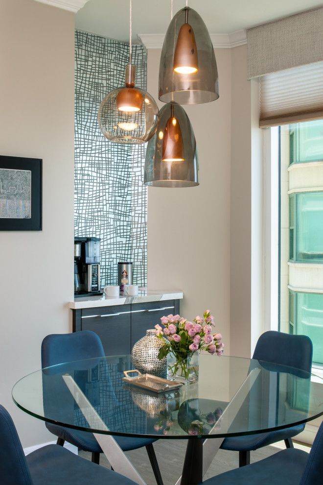 Modern dining area with a glass round table, blue chairs, and pendant lights near a window.