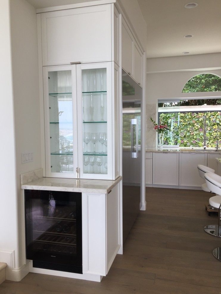 White built-in cabinet with glass shelves and a black wine fridge in a bright open-plan kitchen.