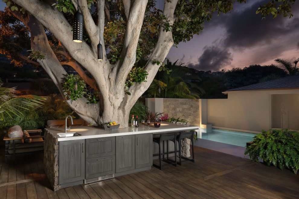 Elegant backyard patio with a large tree, outdoor kitchen, pool, and warm evening lighting