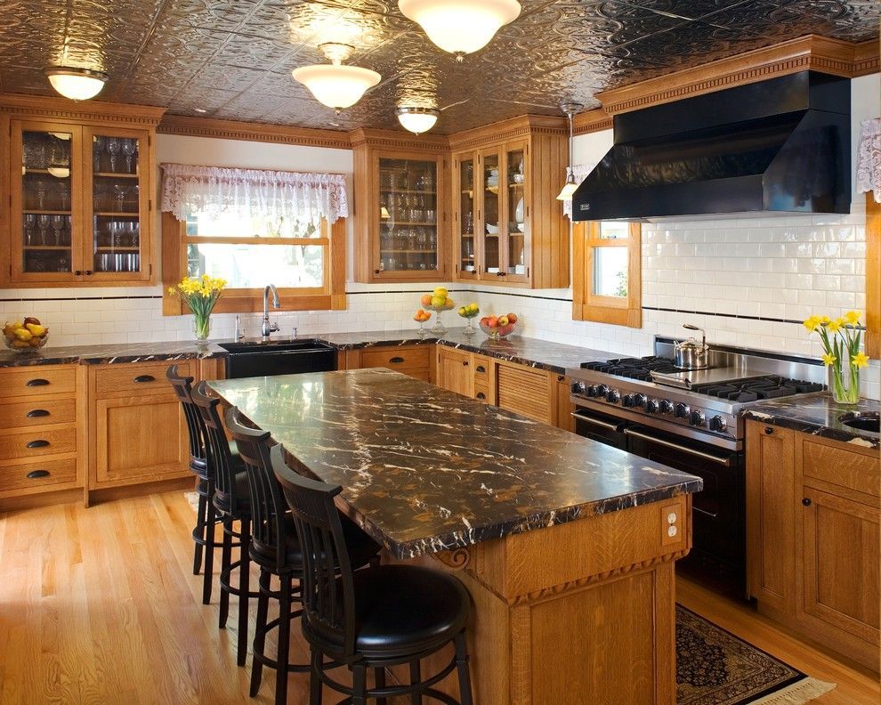 Warm wood kitchen with black marble island, bar stools, hanging lights, and large stove