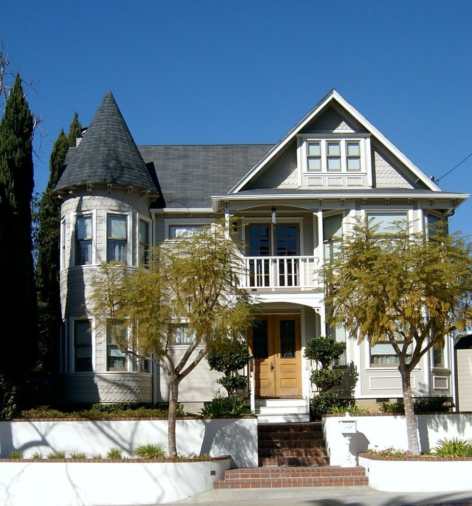Victorian house with a turret and front porch, white trim, and a landscaped front yard under a clear blue sky