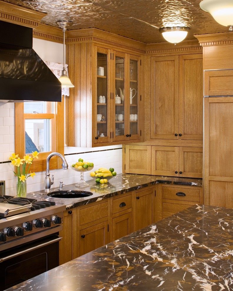 Warm wood kitchen with marble countertop, black stove, glass-front cabinets, and bowls of fruit by the window