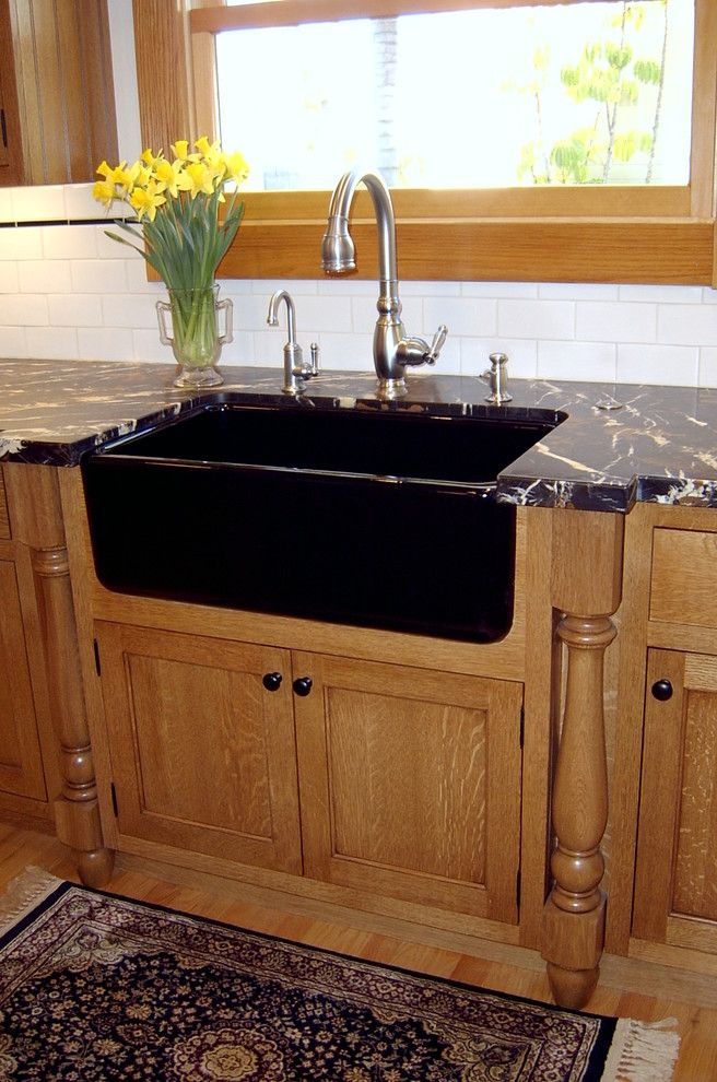 Wooden kitchen sink cabinet with black sink, chrome faucet, and a vase of yellow flowers by the window