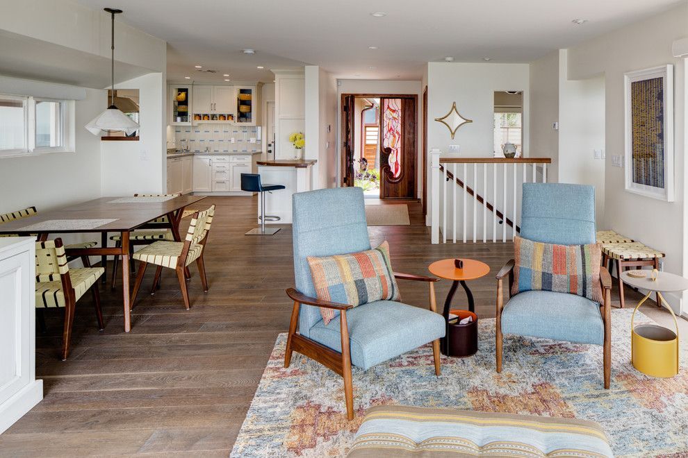 Bright living room with blue armchairs, patterned rug, dining area, and staircase in the background