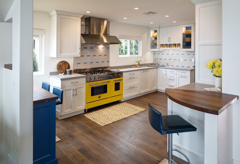 Bright white kitchen with yellow stove, dark wood floor, and small breakfast bar and stool