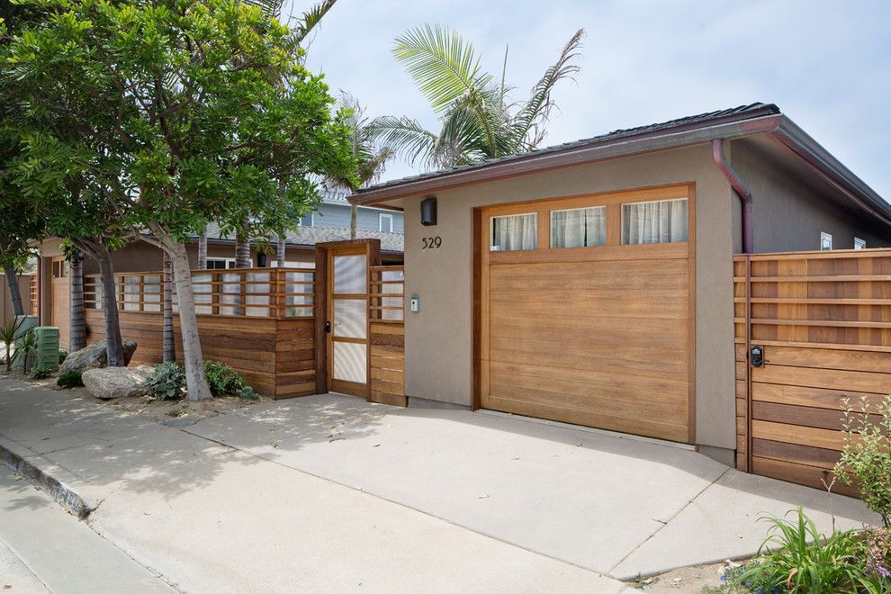 Modern house exterior with wooden garage door, gate, and concrete driveway under trees