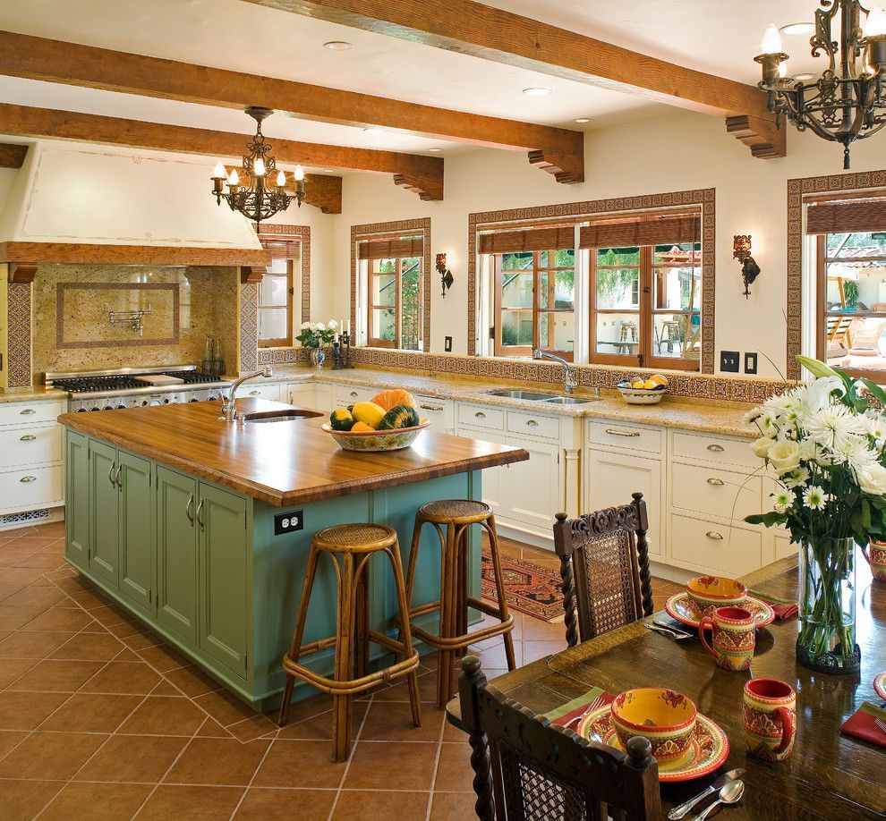 Spacious kitchen with green island, cream cabinets, wood beams, and a dining table by the window.