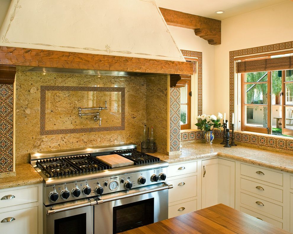 Bright kitchen with stainless steel stove, stone backsplash, white cabinets, and window over the sink
