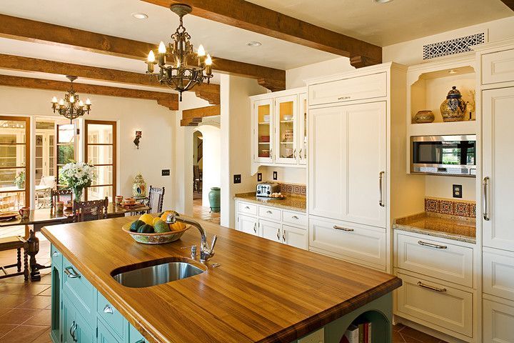 Bright kitchen with wooden island, white cabinets, and chandeliers in a warm, sunlit interior