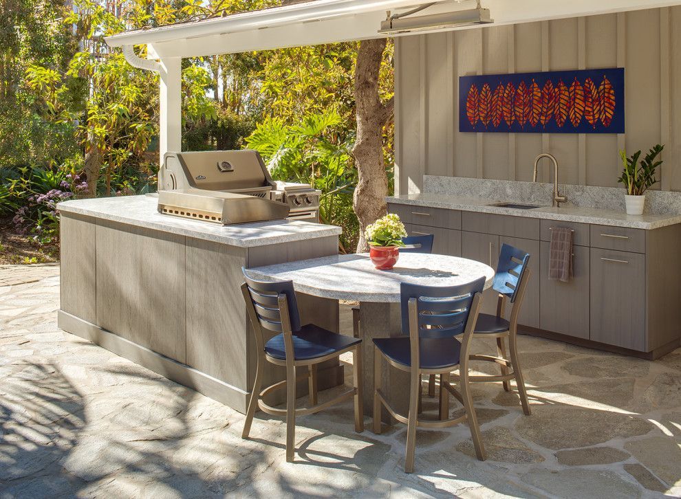 Outdoor kitchen with grill, stone counter, and round table with chairs in a sunny patio garden