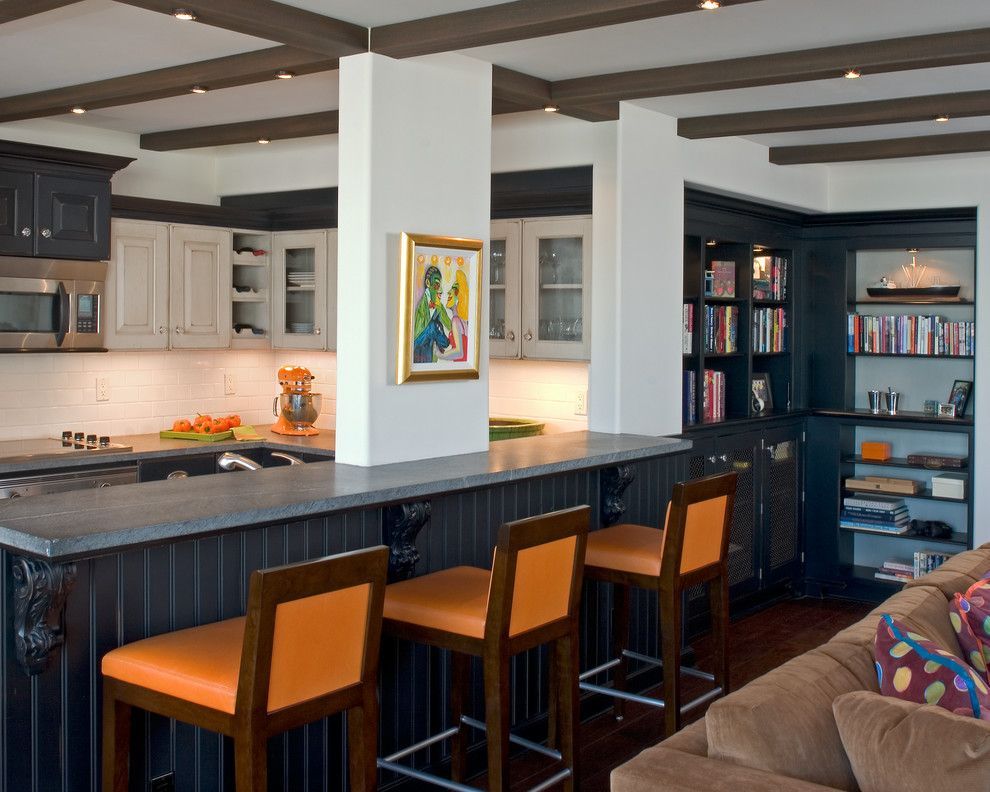 Open kitchen with dark island, orange bar stools, built-in shelves, and a cozy living area beyond