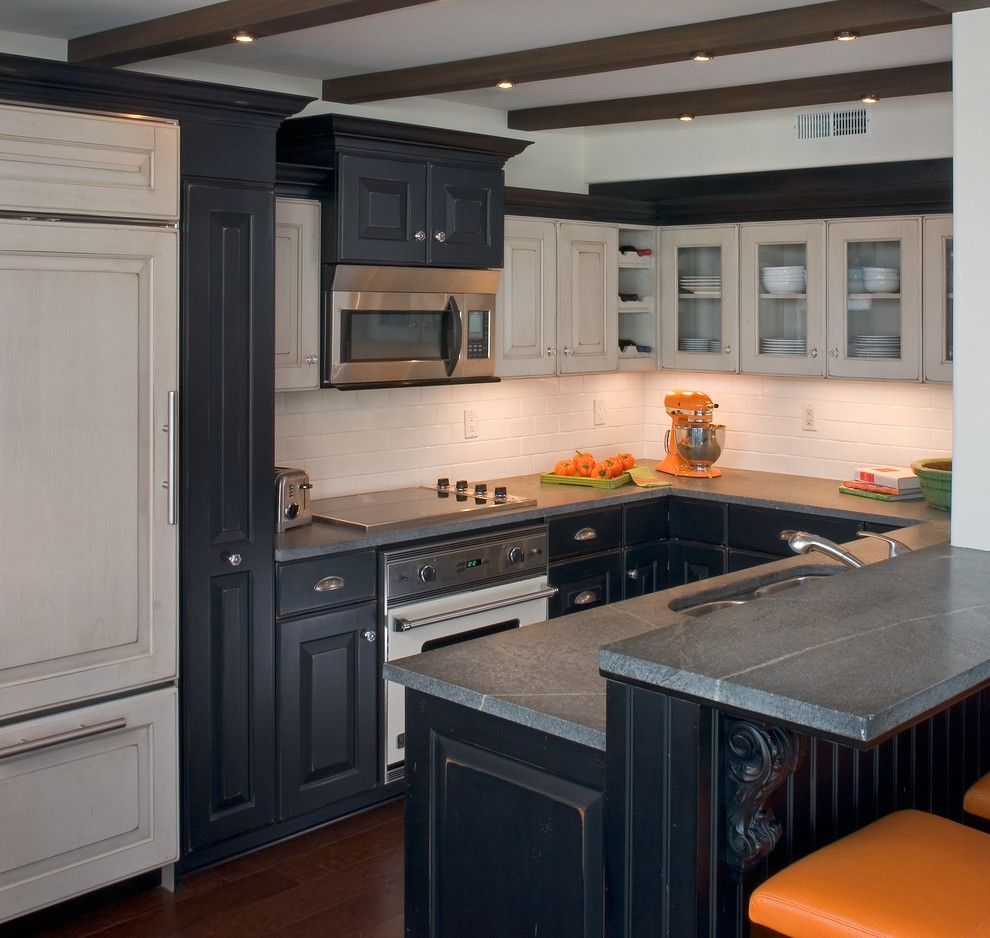Modern kitchen with dark cabinets, white upper cabinets, stainless stove, and black island with orange stools
