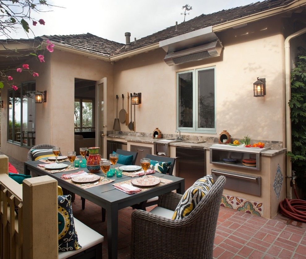 Outdoor patio dining table set with colorful dishes and wicker chairs beside a stucco house
