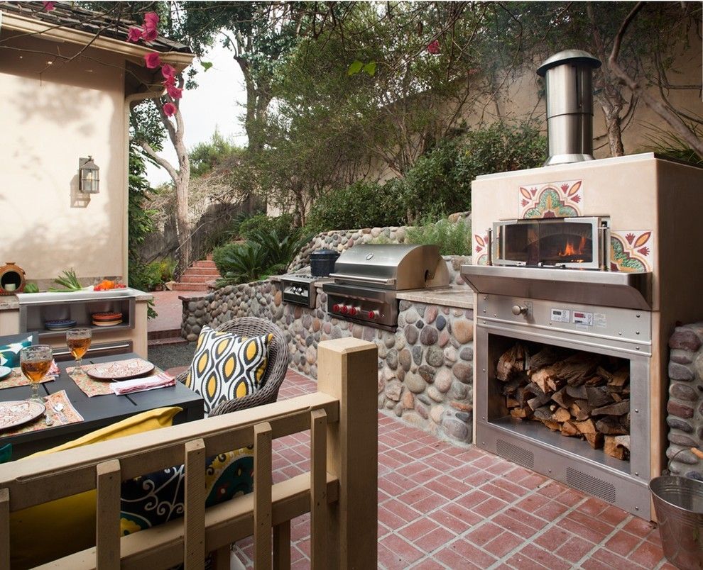 Outdoor patio with brick flooring, built-in grill, pizza oven, and wood-fired fireplace near a table and chairs