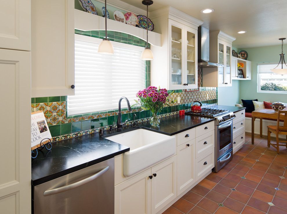 Bright kitchen with white cabinets, dark countertops, green tile backsplash, and a farmhouse sink.