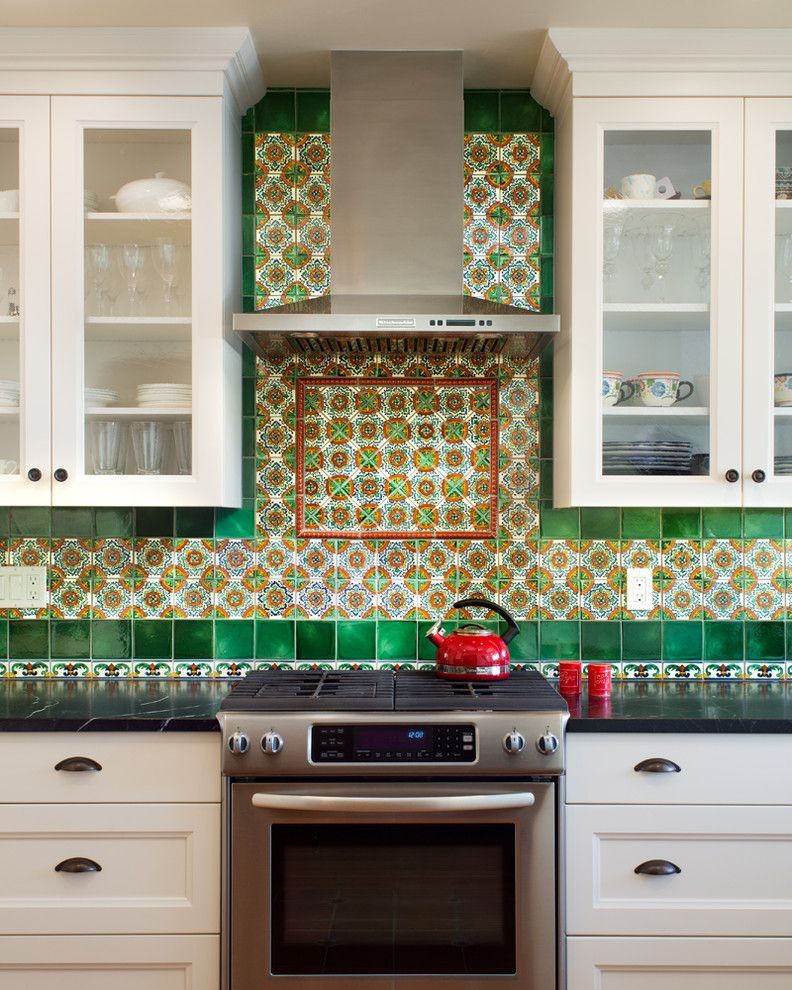 Bright kitchen with green patterned tile backsplash, white cabinets, and a stainless-steel stove and range hood