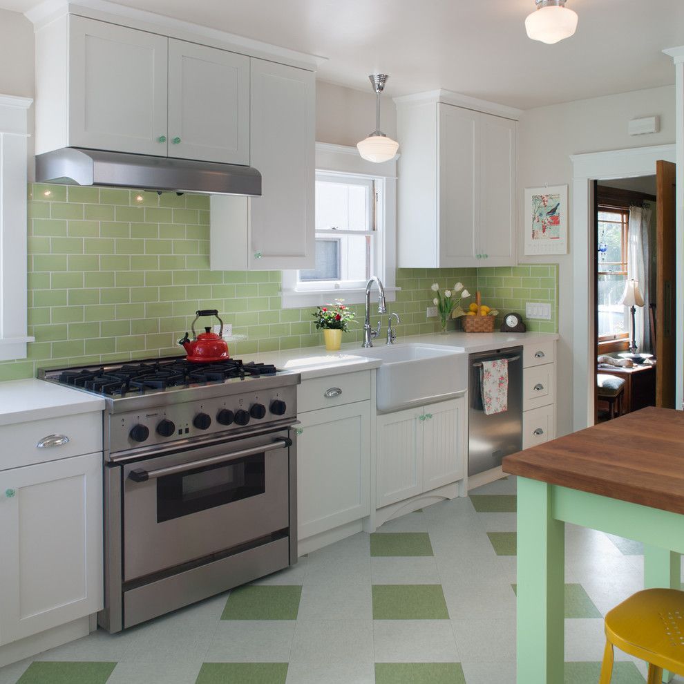 Bright white kitchen with green tile backsplash, stainless stove, farmhouse sink, and wooden island table