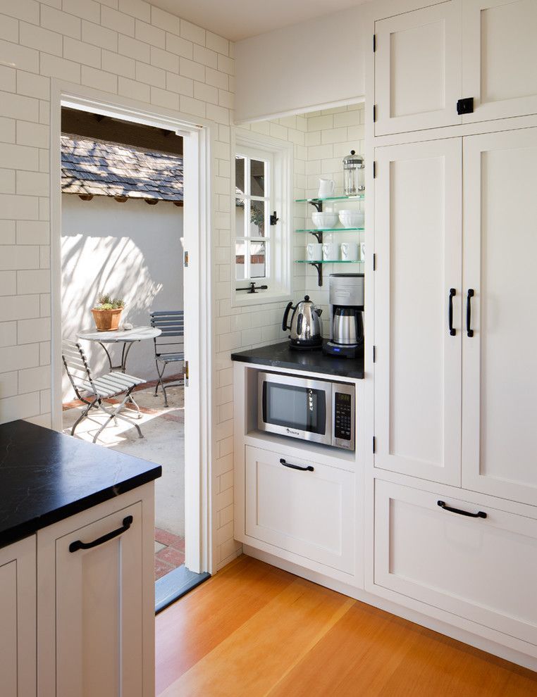 Bright white kitchen with glass shelves, built-in microwave, and open door to a sunny patio.