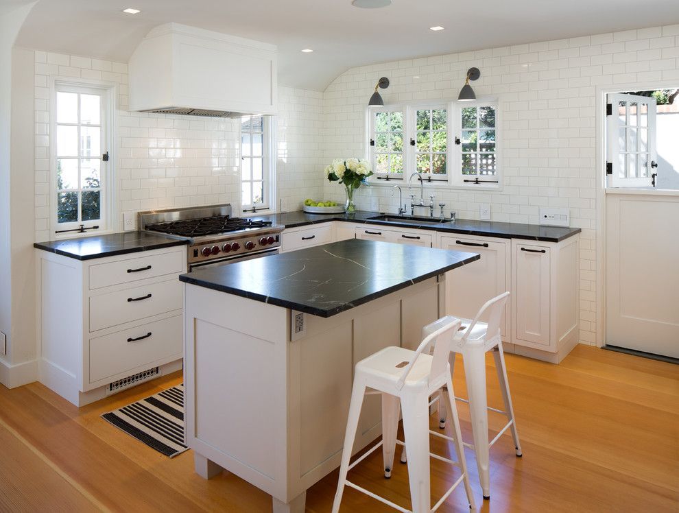 Bright white kitchen with black countertops, central island, and two stools on a wood floor.