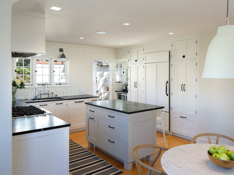 Bright white kitchen with black countertops, island, large cabinets, and a bowl of green apples.