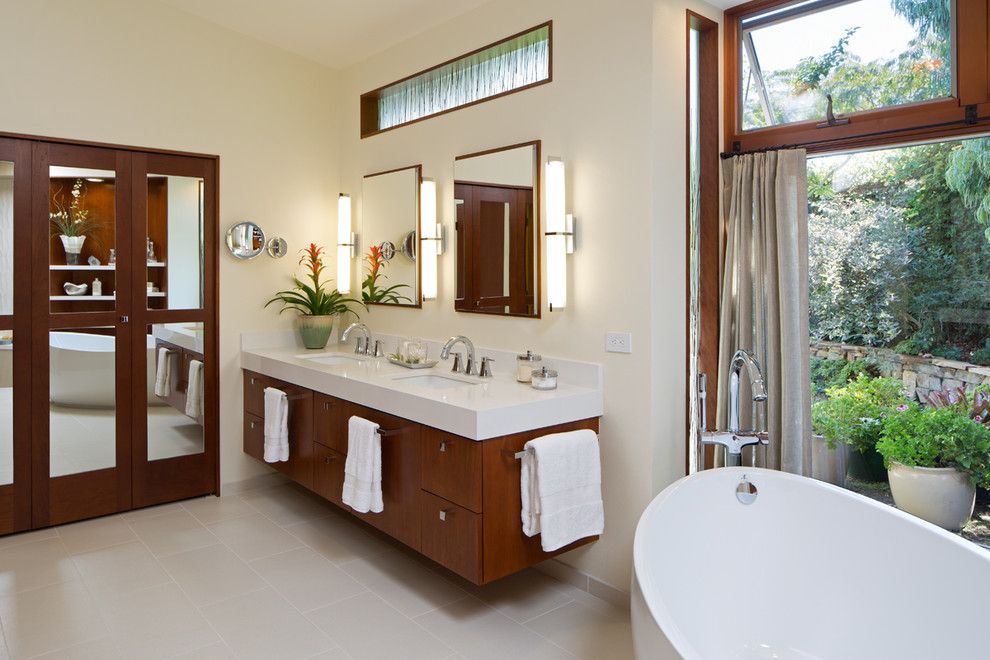 Spacious modern bathroom with double vanity, mirrors, tub, and large windows overlooking greenery
