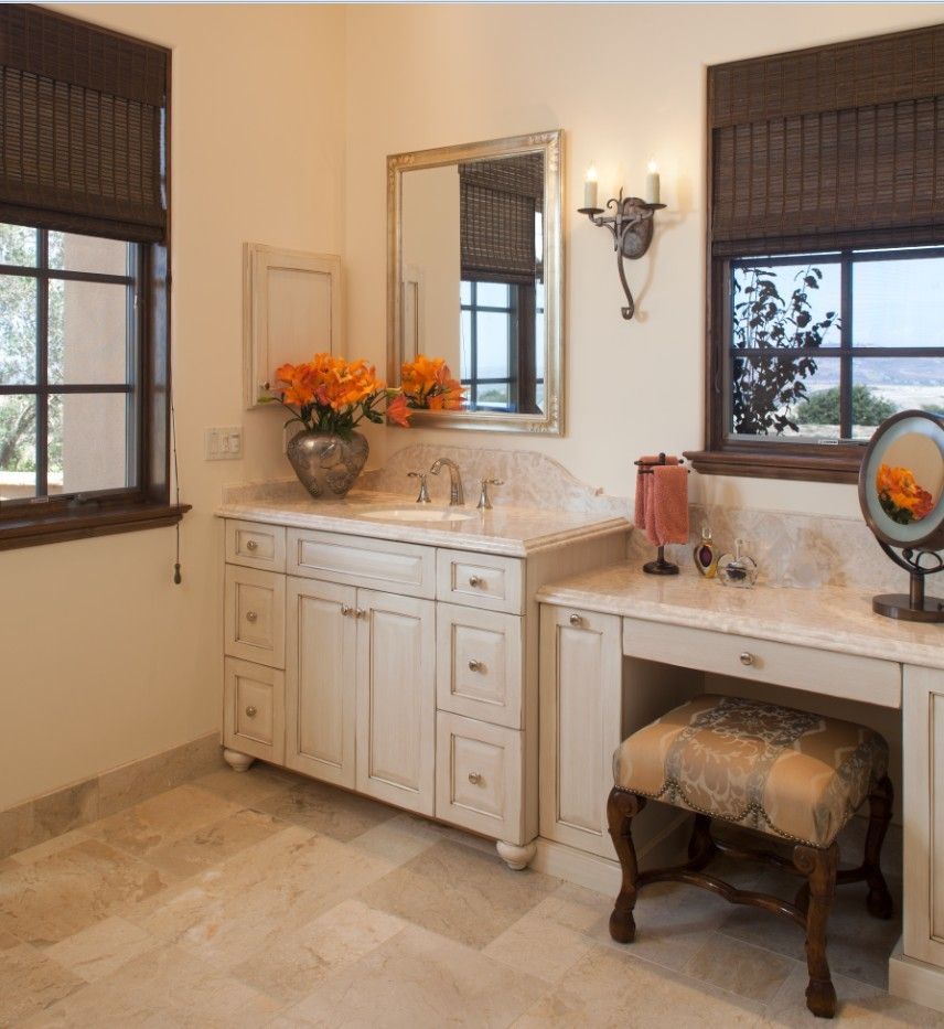 Elegant bathroom vanity with mirror, sconces, flowers, and a cushioned stool by the window