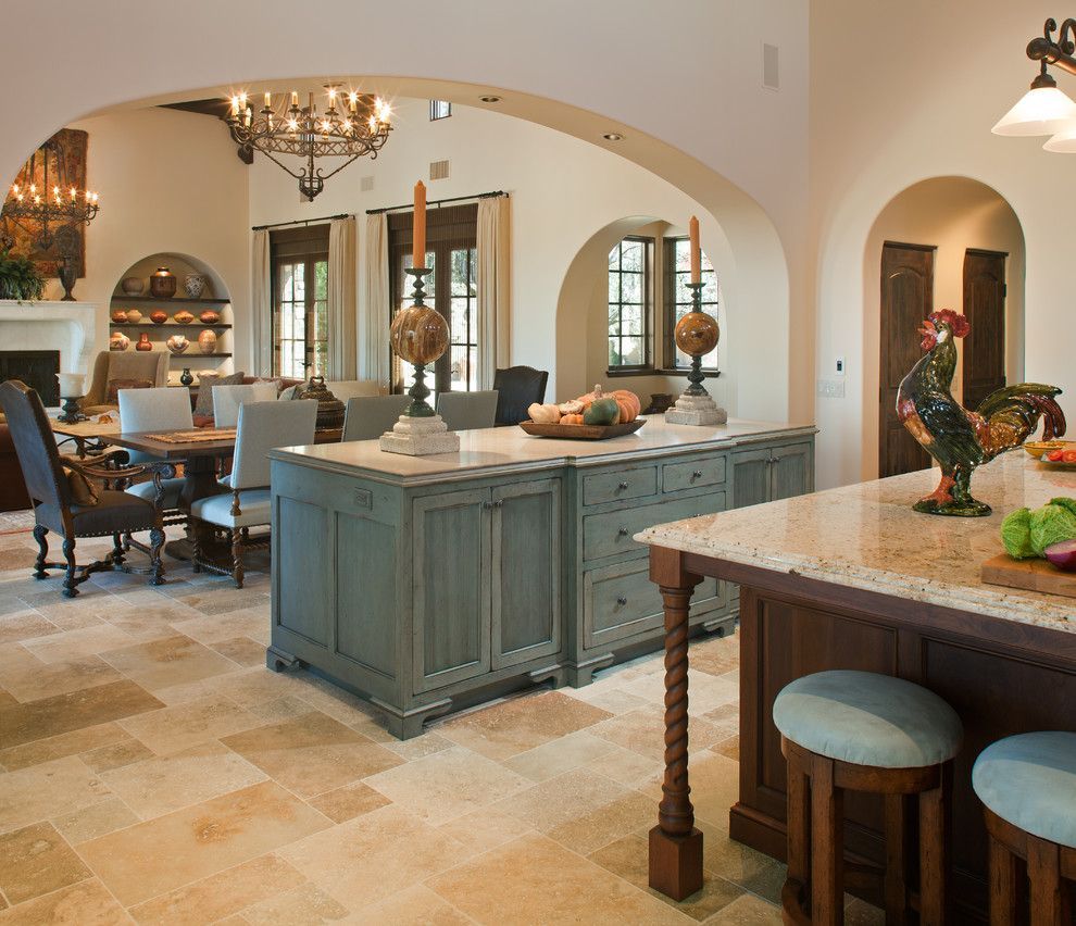 Open kitchen with blue island, stone floors, arched doorway, dining area, and chandelier.