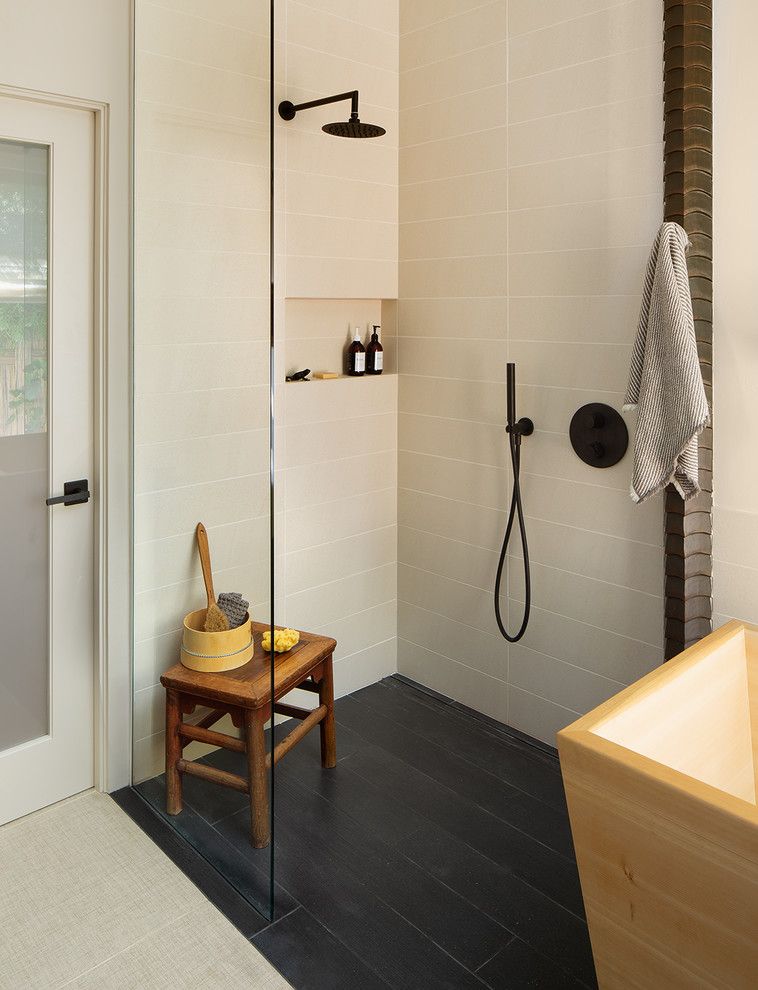 Modern bathroom with black tile shower, wooden stool, and a towel hanging on the wall