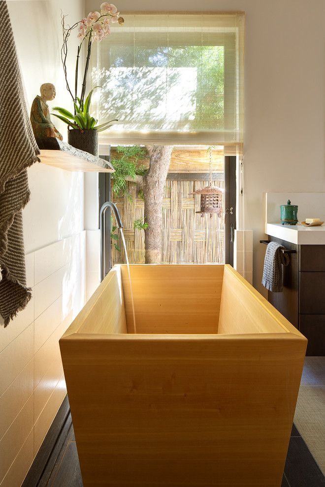 Wooden soaking tub in a bright bathroom beside a window and white sink.
