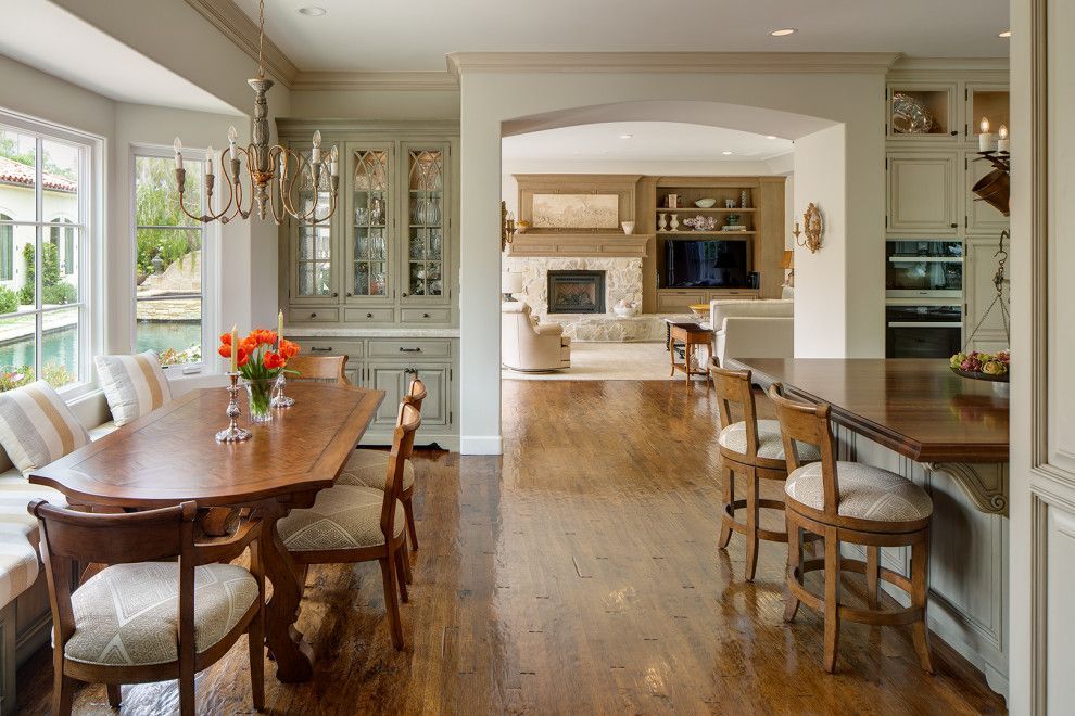Bright dining room with wooden table, chairs, floral centerpiece, and open view to a kitchen.