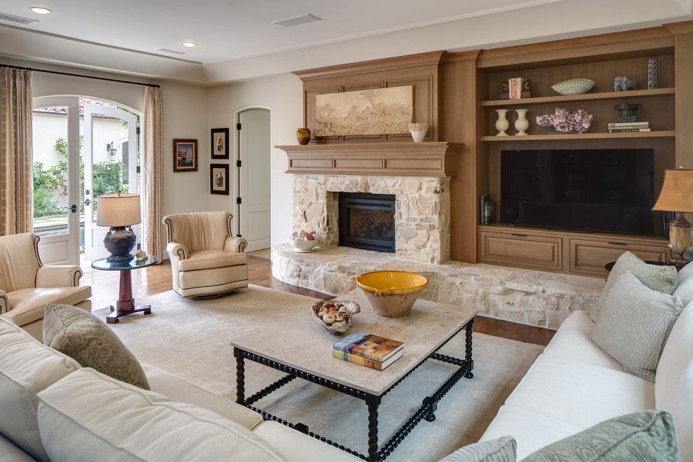 Spacious living room with stone fireplace, built-in TV, and light upholstered seating around a glass coffee table