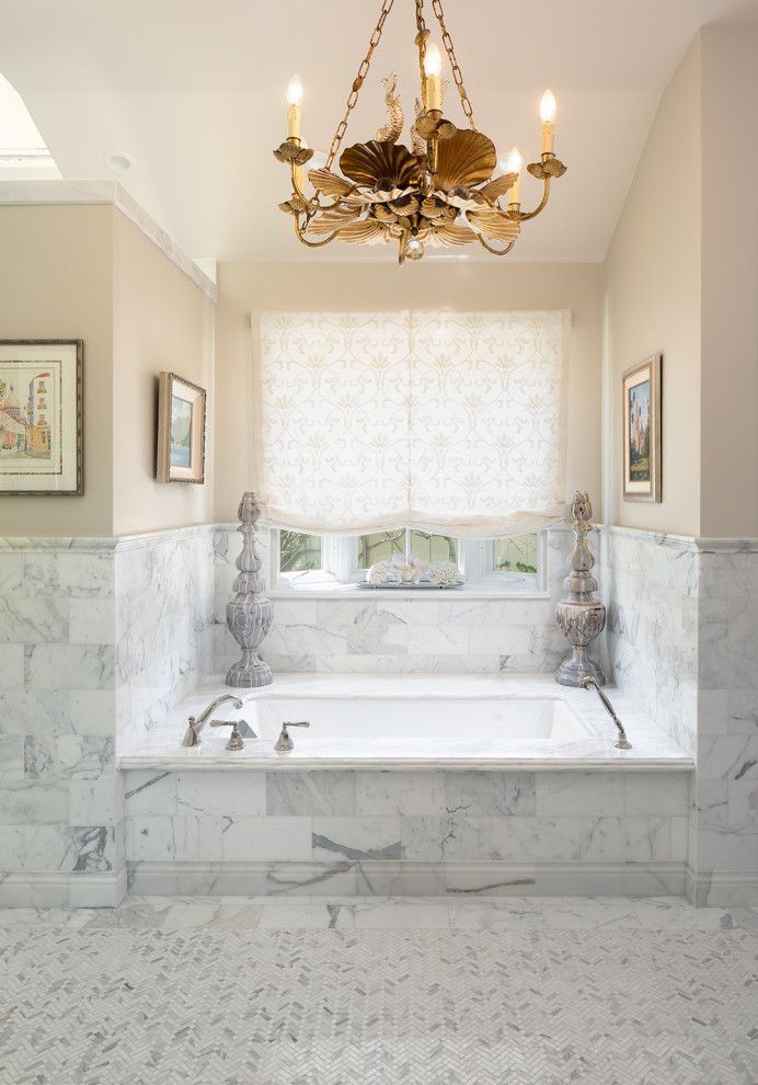 Elegant marble bathroom with a freestanding tub, chandelier, and a window with a sheer shade