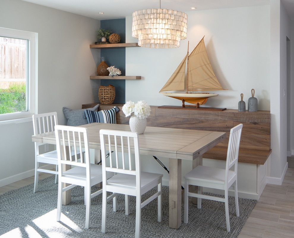 Bright dining nook with white chairs, gray table, built-in bench, shelves, and sailboat decor