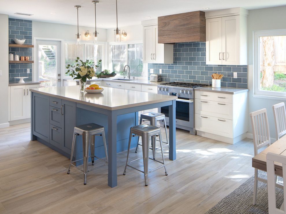 Bright modern kitchen with blue island, white cabinets, pendant lights, and stools by a sunny window.