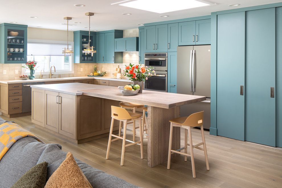Bright modern kitchen with teal cabinets, island, dining stools, and stainless steel appliances