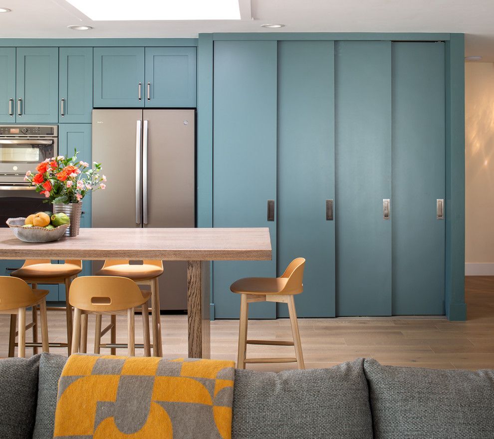 Modern kitchen with teal cabinets, stainless fridge, island stools, and a gray sofa in the foreground