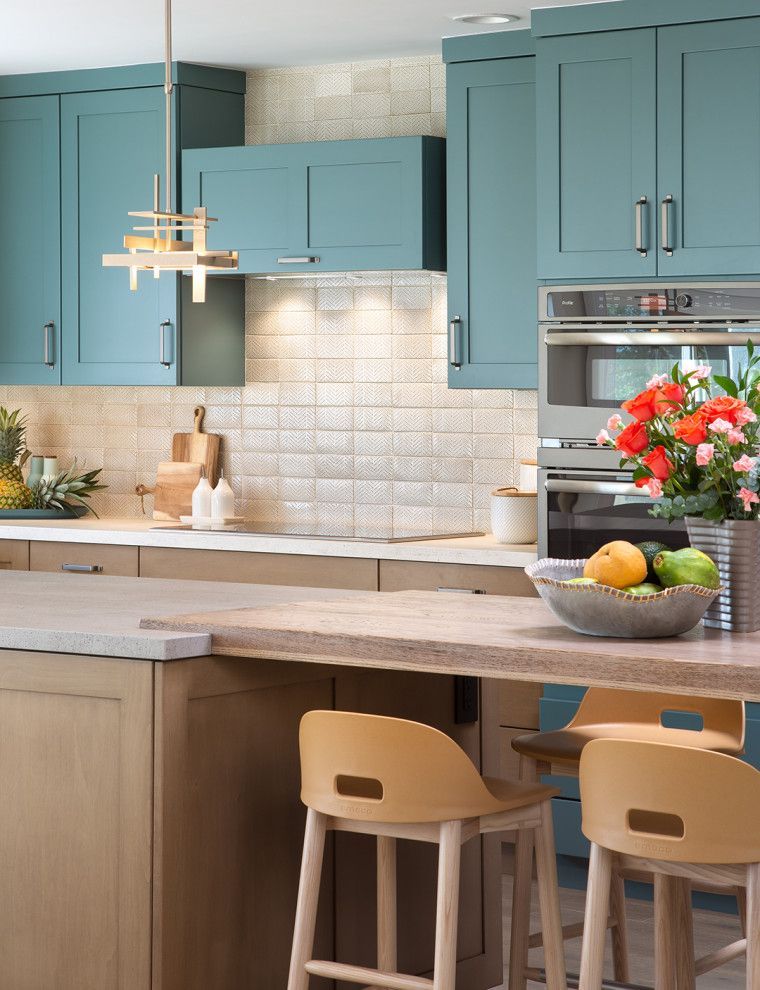 Blue kitchen with white backsplash, wood island, and stools; flowers and fruit on the counter.