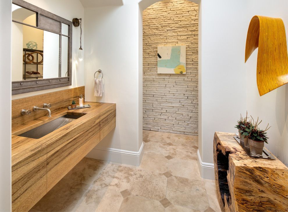 Modern bathroom with wood vanity, stone sink, tiled floor, and textured accent wall.