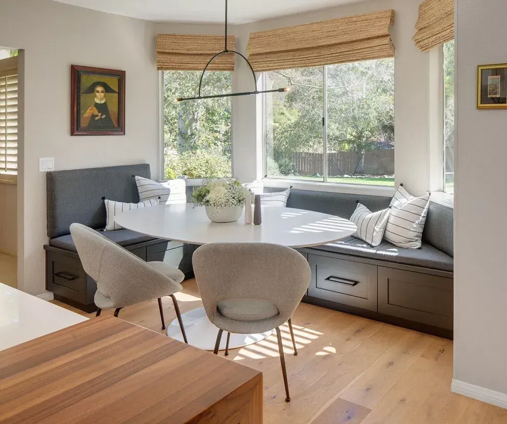 Bright breakfast nook with built-in window seating, round table, and two chairs by a sunlit corner window