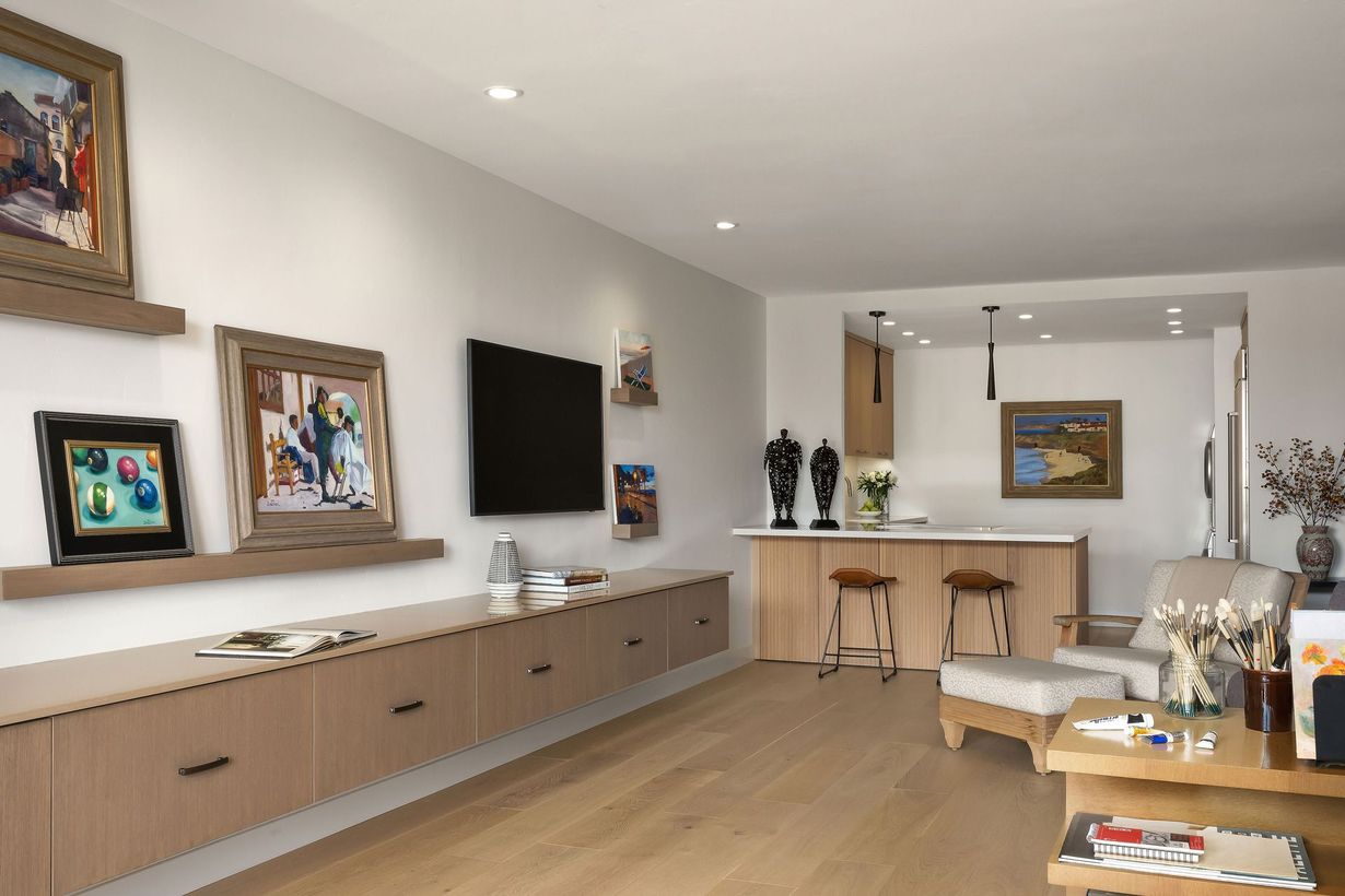 Modern living room with artwork, a TV, a kitchenette, and light wood flooring.