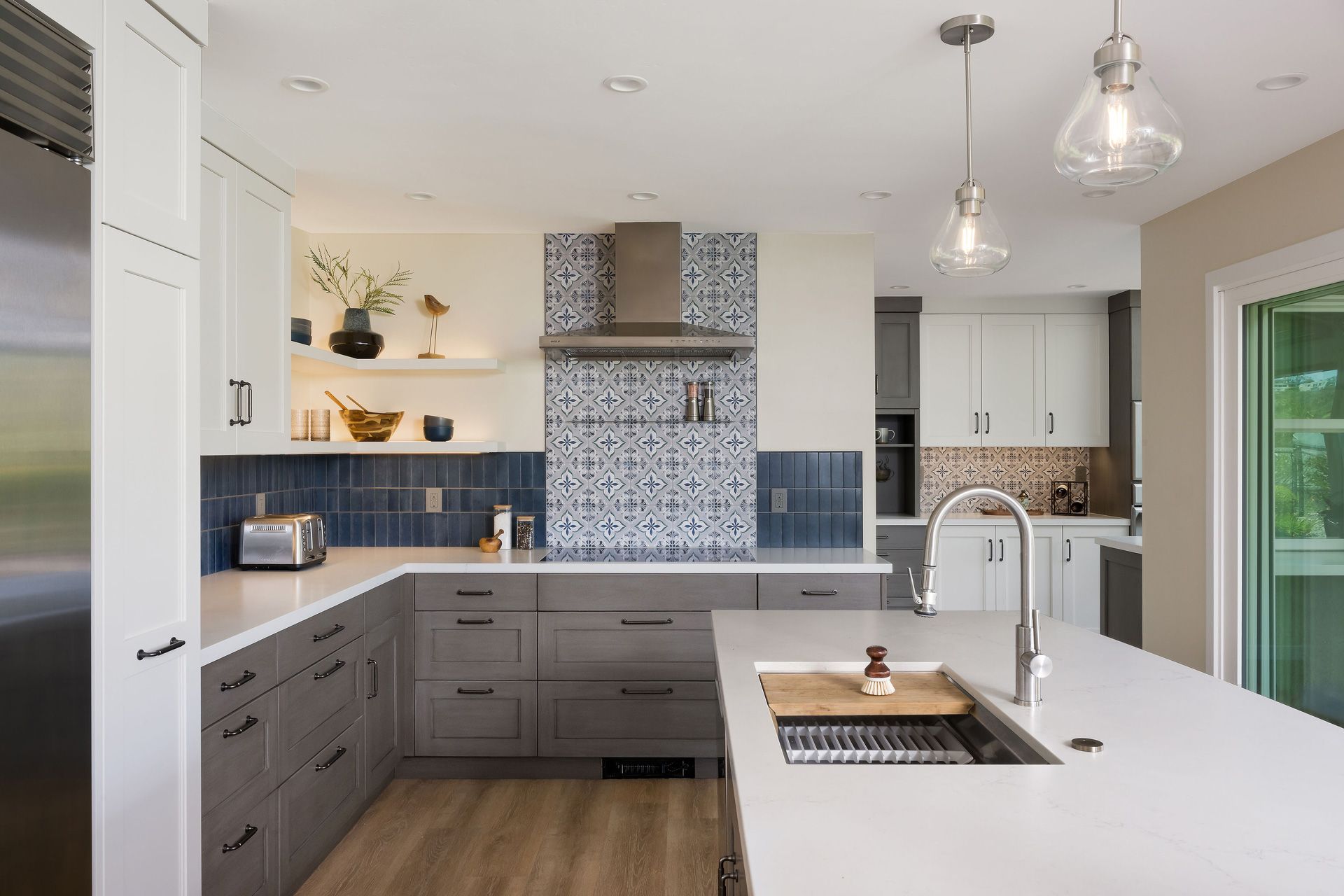 Modern kitchen with gray cabinets, white island, patterned backsplash, and pendant lights