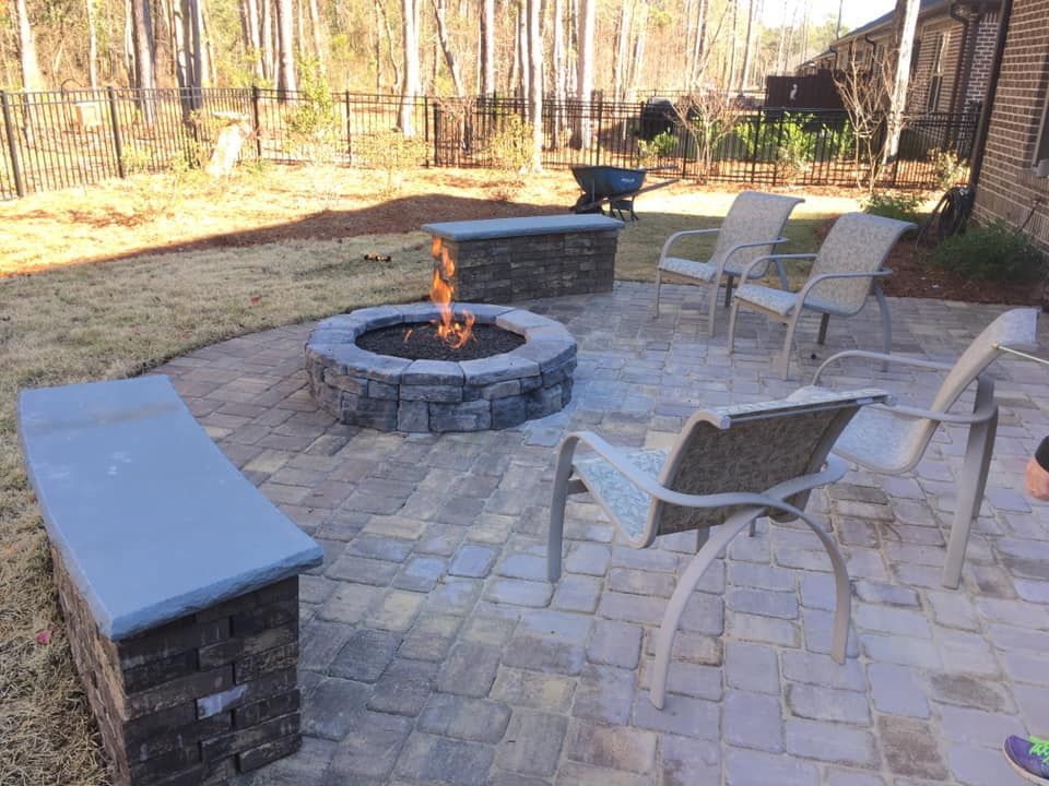 Backyard patio with fire pit, seating, and benches. Flame burning. Brick pavers.