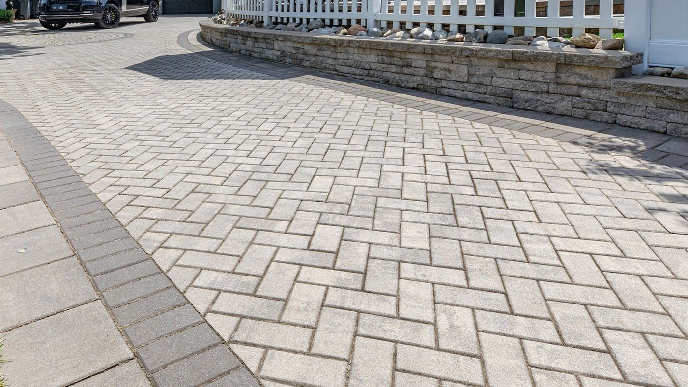 Brick driveway with a herringbone pattern, bordered by gray pavers and a low stone wall.